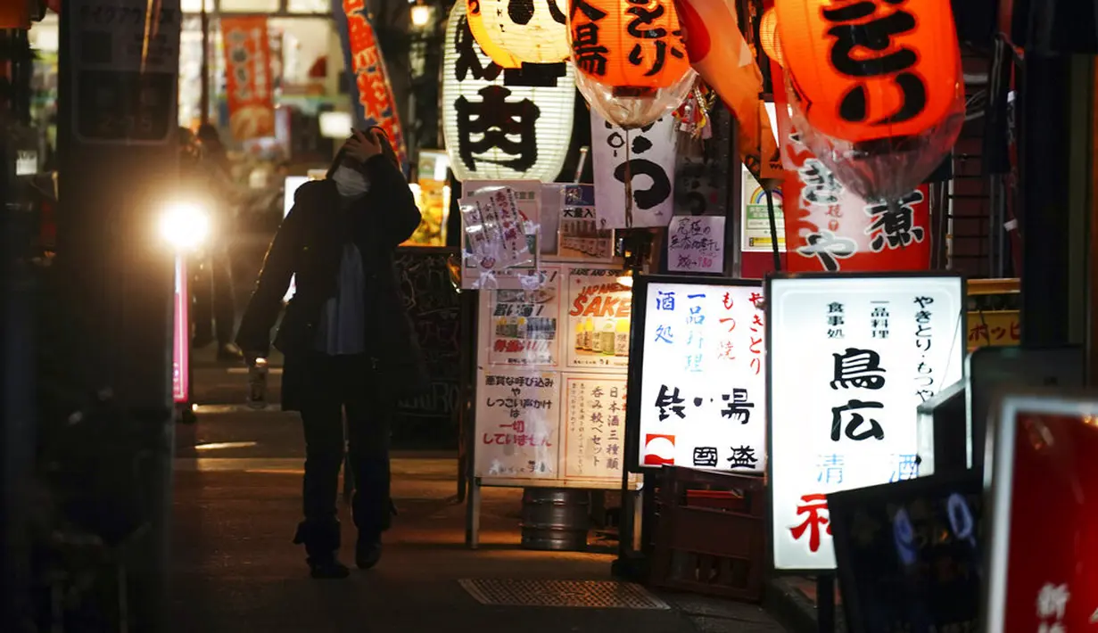 Seorang wanita yang mengenakan masker untuk mengekang penyebaran virus corona COVID-19 berjalan melewati sebuah bar di Tokyo, Jepang, Rabu (6/1/2021). Ibu kota Jepang itu mengkonfirmasi lebih dari 1.500 kasus baru virus corona COVID-19 pada 6 Januari 2021. (AP Photo/Eugene Hoshiko)