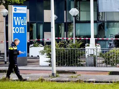 Seorang polisi berjalan dekat sebuah mobil van yang menabrak pintu depan gedung tempat surat kabar ternama Belanda, De Telegraaf di Amsterdam, Selasa (26/6). Akibatnya mobil van itu terbakar dan menyebakan kerusakan pada gedung. (KOEN VAN WEEL/ANP/AFP)