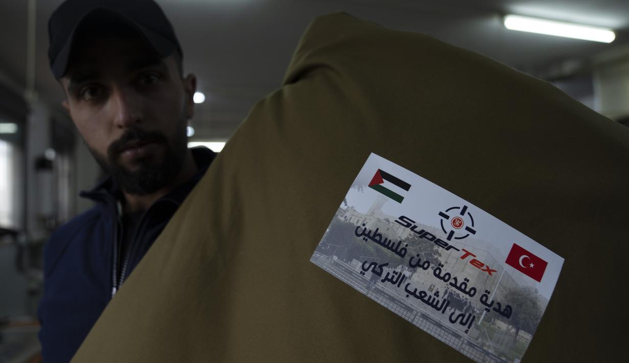 Pekerja memperlihatkan kantong tidur dengan stiker "Sumbangan dari Palestina untuk rakyat Turki", sementara penjahit sedang memproduksi dan menyiapkan pengiriman massal perlengkapan tidur untuk korban gempa bumi di Turki dan Suriah yang sekarang terkena cuaca musim dingin yang membekukan, di kota Hebron, Tepi Barat, Kamis (16/2/2023). Warga Palestina telah turun tangan untuk membantu mereka yang terguncang akibat gempa dahsyat di Turki dan Suriah. (AP Photo/Nasser Nasser)