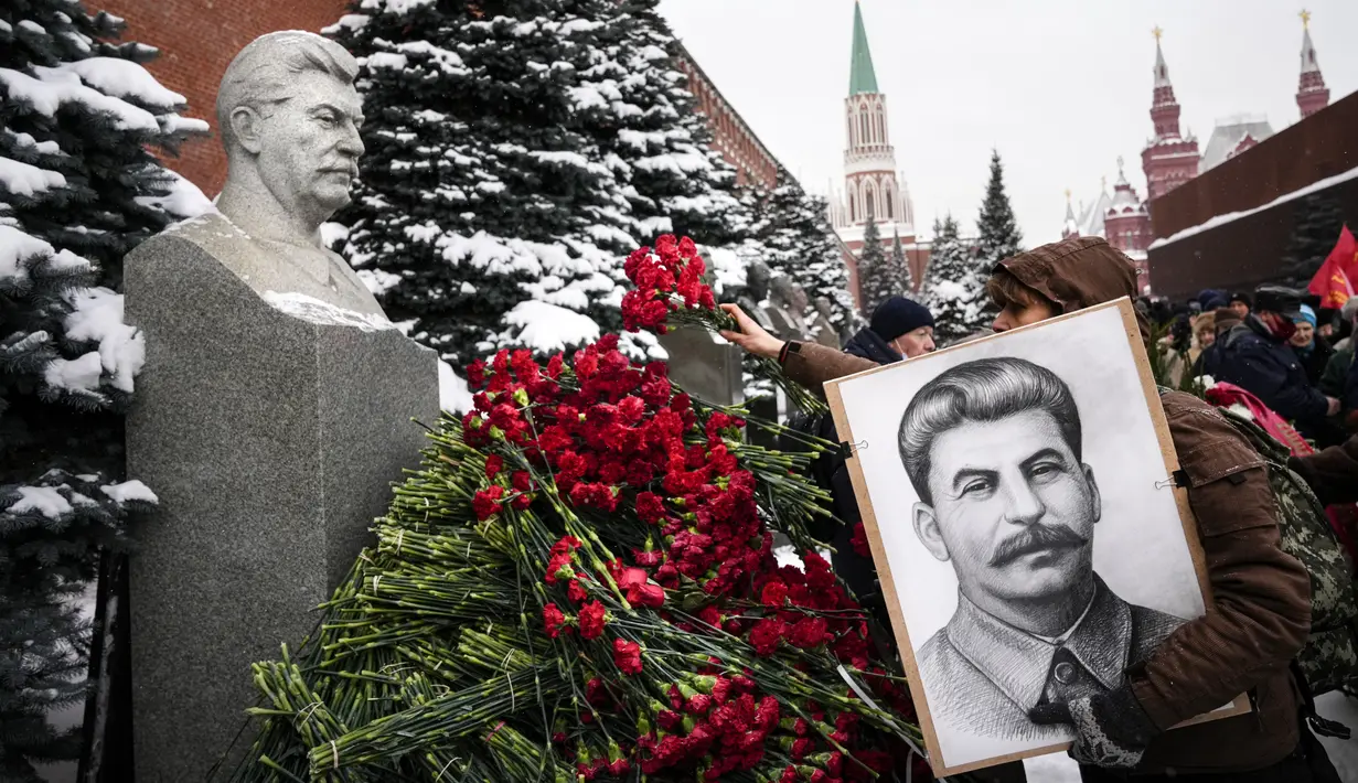 Seorang wanita memegang potret pemimpin Soviet Josef Stalin sambil meletakkan bunga di makamnya untuk memperingati 142 tahun kelahirannya di dekat Tembok Kremlin di Lapangan Merah di Moskow, Rusia, Selasa (21/12/2021). (AP Photo/Alexander Zemlanichenko)