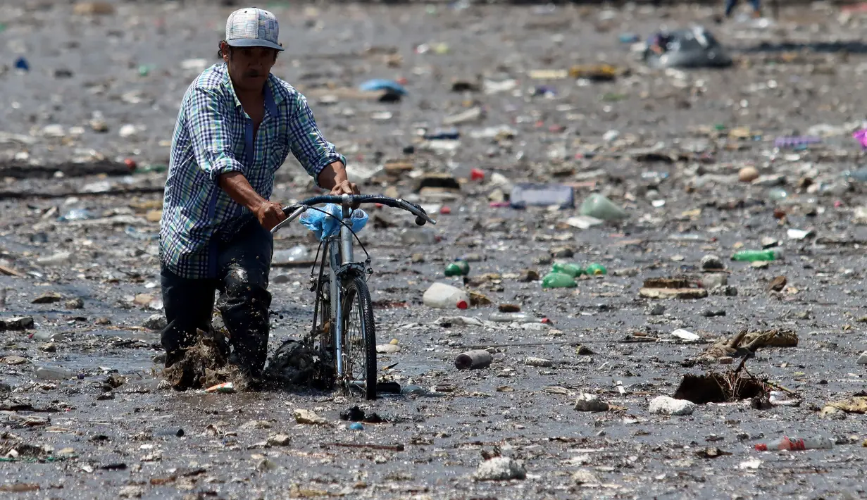 Seorang pria mendorong sepeda di sepanjang jalan yang berlumpur setelah aliran El Seco meluap akibat hujan lebat di Zapopan, Jalisco State, Meksiko (26/7/2021). Luapan sungai menyebabkan banjir disertai lumpur dan sampah melanda Zapopan, kota di negara bagian Jalisco, Meksiko. (AFP/Ulises Ruiz)