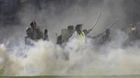 Petugas polisi dan tentara berdiri di tengah asap gas air mata setelah berusaha membubarkan penonton yang memasuki lapangan Stadion Kanjuruhan, Malang, Jawa Timur, Indonesia, Sabtu, 1 Oktober 2022. (AP/Yudha Prabowo)