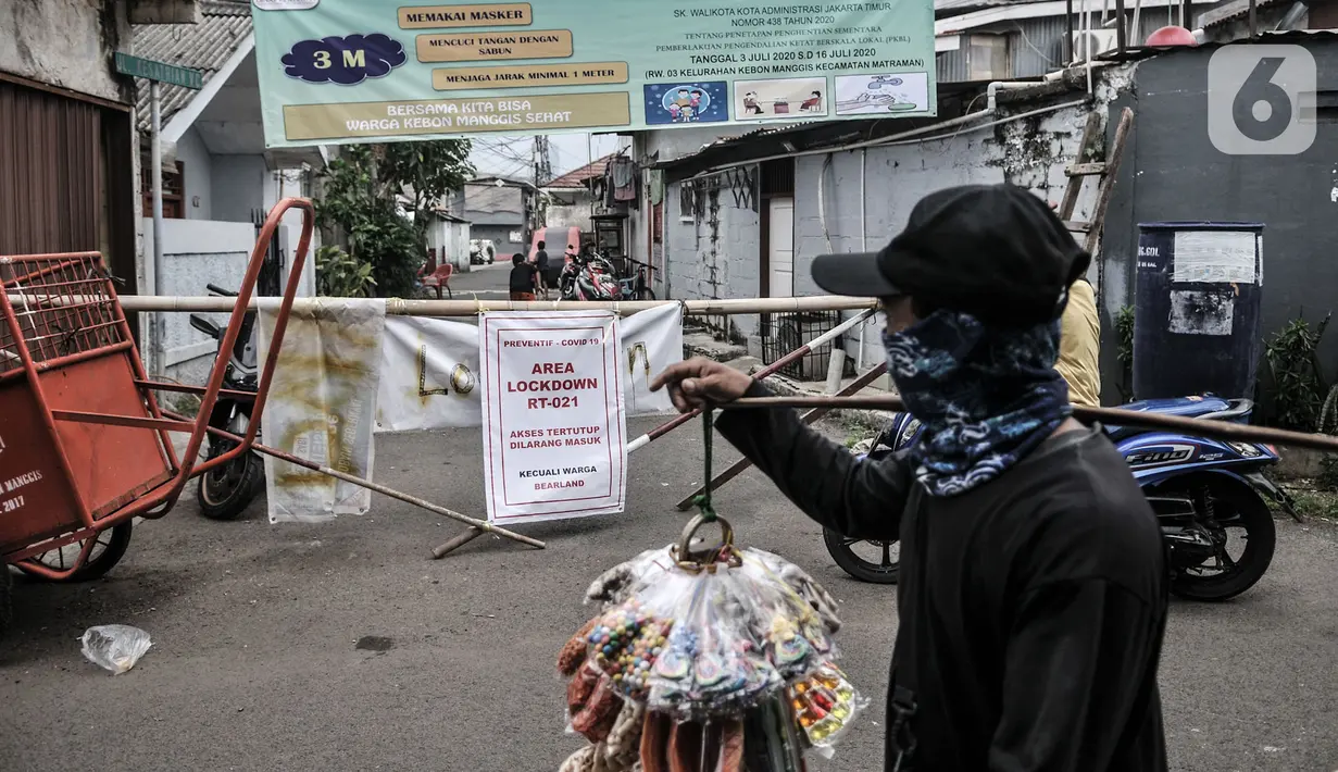 Pedagang melintas di depan jalan permukiman yang ditutup usai ditetapkan sebagai Zona Merah Covid-19 di RW 03 Kelurahan Kebon Manggis, Jakarta, Selasa (14/7/2020). Jumlah RW yang masuk dalam zona merah Covid-19 di DKI Jakarta kembali bertambah menjadi 30 RW. (Mmerdeka.com/Iqbal Nugroho)