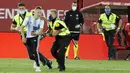 Sejumlah petugas keamanan berusaha menangkap seorang fans yang nekat menerobos lapangan saat pertandingan antara Mallorca melawan Barcelona di Stadion Son Moix, Minggu (14/6/2020). Fans tersebut ingin berfoto dengan Lionel Messi. (AP/Francisco Ubilla)