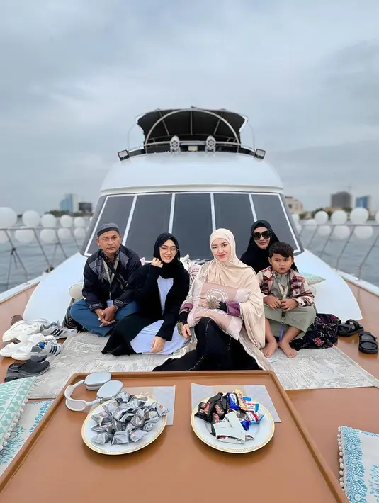 Potret bahagia Happy Salma bersama keluarganya di atas kapal. Happy Salma yang berpose di tengah tampil anggun dengan abay hitam, ditumpuk lagi dengan atasan cokelat muda yang serasi dengan hijabnya. [Foto: Instagram/happy_asmara77]