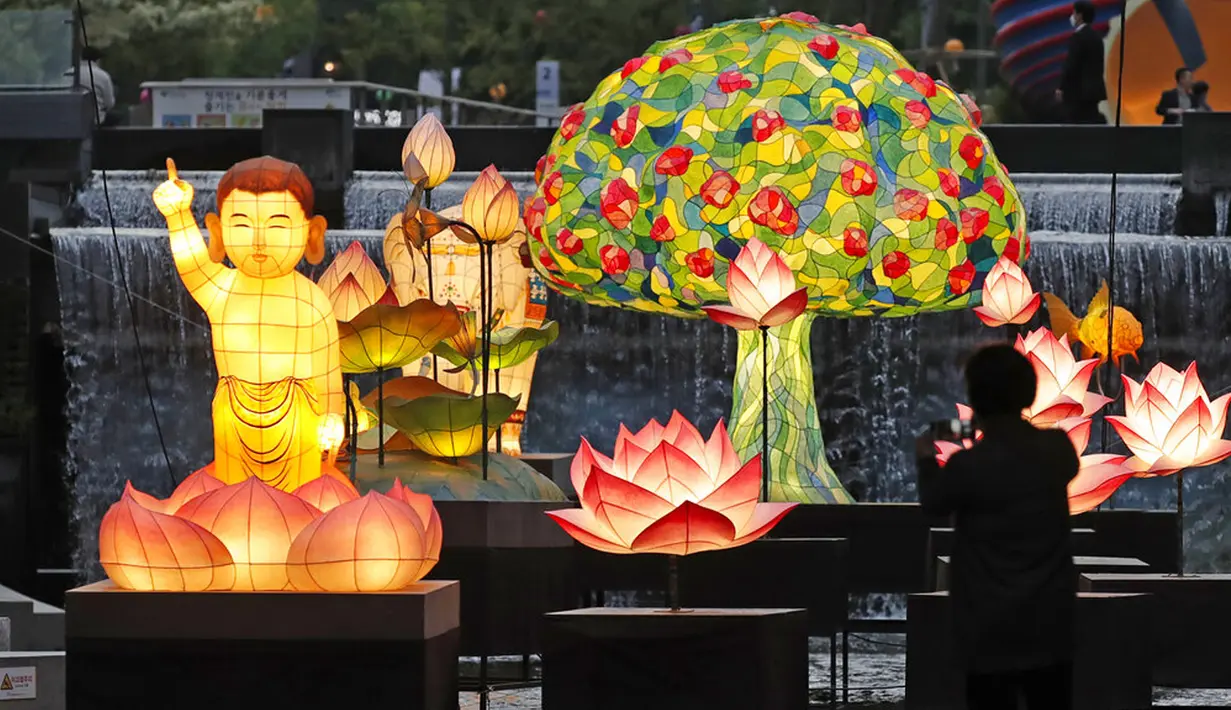 Seorang pengunjung yang mengenakan masker wajah sebagai tindakan pencegahan terhadap penyebaran virus corona COVID-19 berdiri dekat lentera yang dipajang untuk perayaan ulang tahun Buddha pada 19 Mei mendatang di Seoul, Korea Selatan, Senin (10/5/2021). (AP Photo/Lee Jin-man)