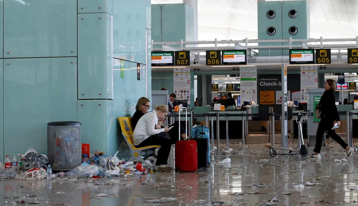 Penumpang memainkan ponsel di antara sampah yang berserakan di Bandara Barcelona, Spanyol, Kamis (1/12). Para petugas kebersihan melakukan aksi protes mengotori ruangan bandara dengan sampah sobekan kertas. (REUTERS/Albert Gea)
