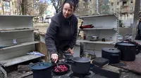 Seorang perempuan memasak di halaman gedung apartemen yang rusak akibat tembakan dari pertempuran di pinggiran Mariupol, Ukraina, di wilayah di bawah kendali pemerintah separatis Republik Rakyat Donetsk, pada Selasa, 29 Maret 2022. (AP Photo/Alexei Alexandrov )