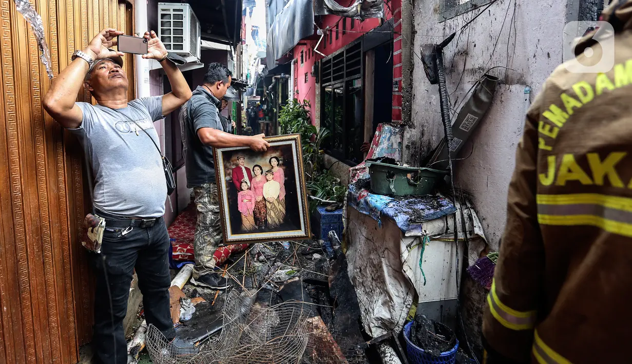 Seorang pria mengabadikan petugas pemadam kebakaran yang melakukan proses pendinginan pada permukiman penduduk yang terbakar di Jalan Masjid Alhuda atau depan Stasiun Kebayoran Lama RT 05/01, Jakarta Selatan, Selasa (24/5/2022). Tidak ada korban jiwa dalam kebakaran yang menghanguskan sekitar 20 rumah tersebut. (Liputan6.com/Johan Tallo)
