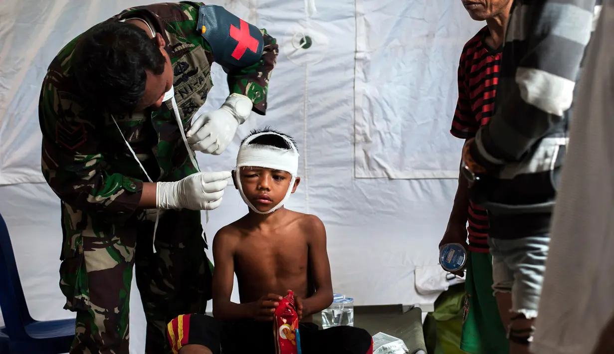 Petugas medis militer mengobati seorang anak laki-laki yang mengalami cedera akibat gempa Lombok di rumah sakit darurat di Kayangan, Rabu (8/8). BPBD Lombok Utara mencatat data sementara jumlah korban jiwa mencapai 347 orang. (AP/Fauzy Chaniago)