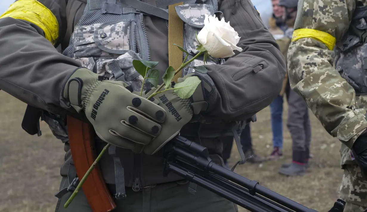 Seorang anggota Pasukan Pertahanan Teritorial Ukraina memegang bunga selama upacara pernikahan untuk Lesia Ivashchenko dan Valerii Fylymonov di pos pemeriksaan di Kiev, 6 Maret 2022. Kedunya menikah dengan upacara seadanya yang dilakukan korps mereka di tengah invasi Rusia. (AP/Efrem Lukatsky)