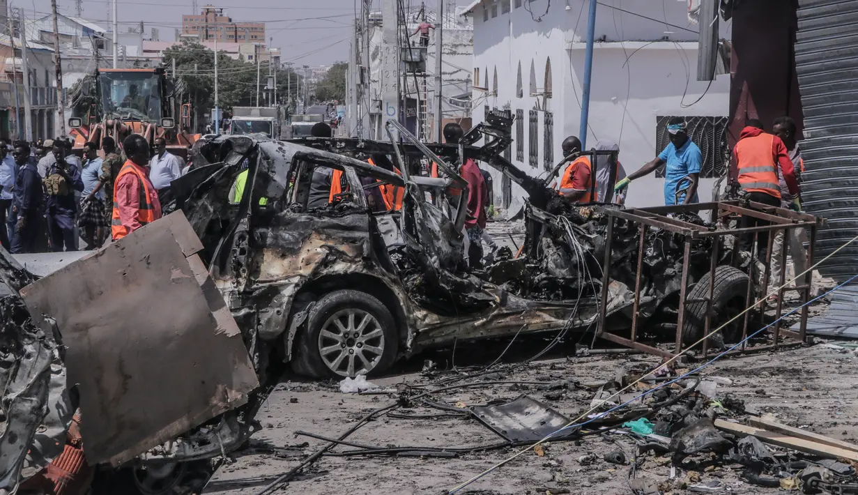 Tim penyelamat dan pengamat berkumpul di dekat puing-puing di lokasi serangan bom mobil bunuh diri di dekat pos pemeriksaan keamanan di Mogadishu, Somalia (13/2/2021). Rentetan tembakan juga berulang kali terdengar setelah ledakan di saat jam sibuk tersebut. (Abdirazak Hussein FARAH / AFP)