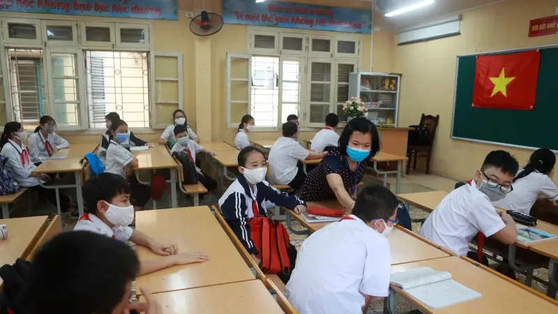 Seorang guru memeriksa suhu murid-muridnya sebelum memulai kelas di sekolah menengah Dinh Cong di Hanoi pada hari Senin. Siswa di seluruh Vietnam kembali bersekolah setelah tiga bulan belajar online.