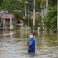 Seorang pria mengarungi jalan yang banjir di Hulu Langat, di luar Kuala Lumpur, Malaysia, Minggu (19/12/2021). Kuala Lumpur dan perkampungan sekitarnya dilanda banjir akibat hujan deras selama dua hari, menyebabkan ribuan warga mengungsi dan banyak jalan yang memutus akses. (AP Photo/Vincent Thian)