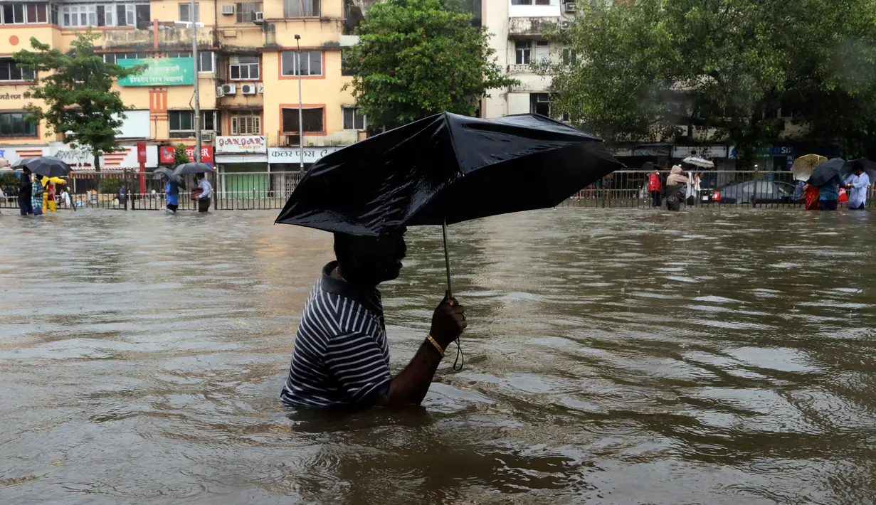 Seorang pria menggunakan payung sambil berjalan melewati banjir yang merendam kota Mumbai, India, Selasa (29/8). Hujan lebat yang terus-menerus mengguyur Mumbai mengakibatkan banjir di beberapa daerah di kota tersebut. (AP Photo/Rajanish Kakade)
