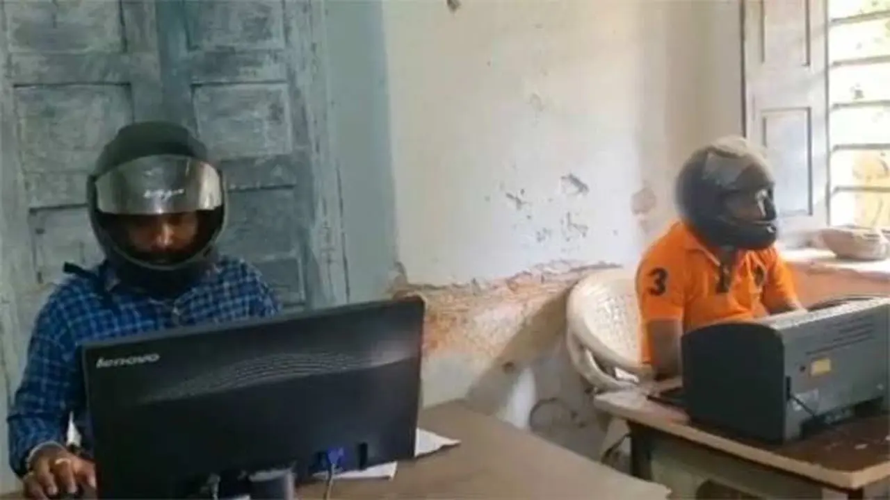 Pegawai di India mengenakan helm sepeda motor sebagai pelindung kepala dari puing yang terjatuh.