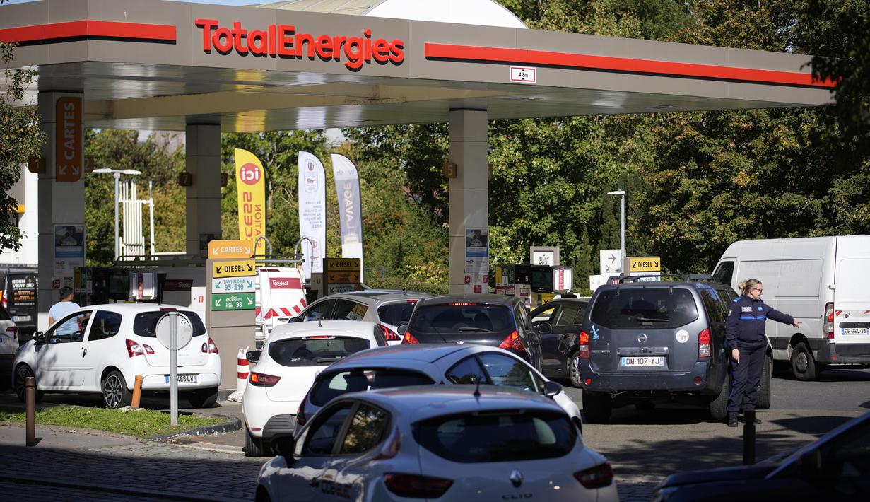 Seorang petugas polisi mengarahkan mobil saat pengemudi berbaris di sebuah pompa bensin di Paris, Selasa (11/10/2022). Selain aksi mogok kerja, harga BBM mengalami kenaikan dalam tujuh hari terakhir. (AP Photo/Christophe Ena)