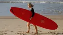 Seorang wanita membawa papan selancar bersiap bermain saat pembatasan sosial Covid-19 mulai dilonggarkan di Pantai Bondi di Sydney, Selasa, (28/4/2020).  Pantai ini terbuka untuk perenang dan peselancar untuk berolahraga saja. (AP Photo/Rick Rycroft)