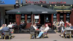 Pelanggan duduk di teras sebuah kafe di Amsterdam, Rabu (28/4/2021). Pemerintah Belanda mulai melonggarkan pembatasan ketat terkait Covid-19, mengakhiri jam malam yang kontroversial dan mengizinkan kafe untuk buka di luar ruangan. (REMKO DE WAAL/ANP/AFP)