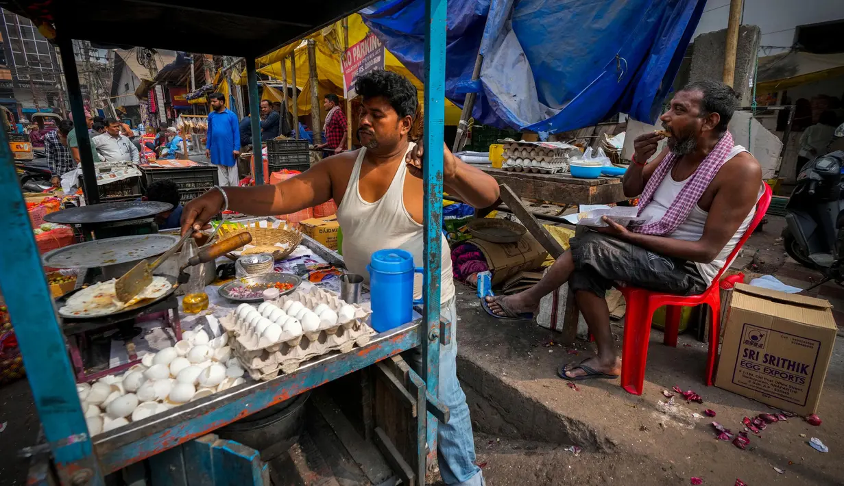 Seorang pedagang kaki lima menyiapkan makanan saat seorang pria makan di sebuah pasar grosir sayuran di Guwahati, India, Rabu (1/2/2023). Pemerintah Perdana Menteri India Narendra Modi meningkatkan belanja modal sebesar 33% untuk memacu pertumbuhan ekonomi dan menciptakan lapangan kerja menjelang pemilihan umum tahun depan. (AP Photo/Anupam Nath)