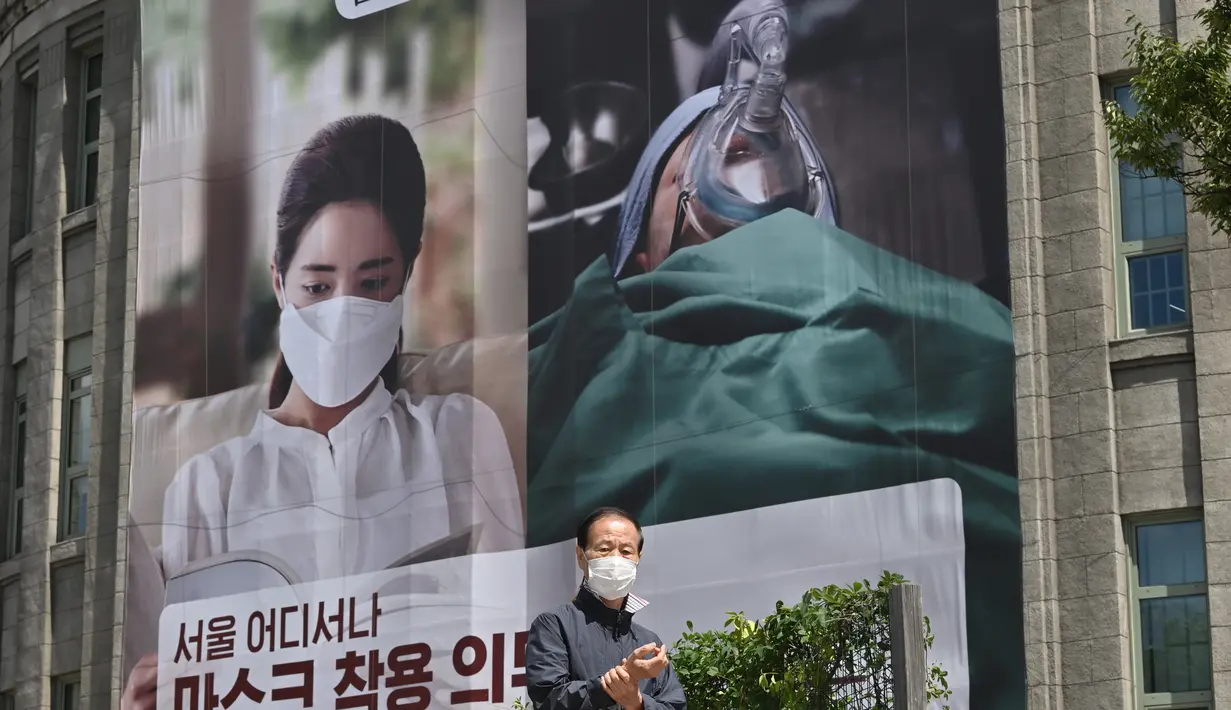 Seorang pria berjalan melewati spanduk yang menganjurkan wajib mengenakan topeng di depan Balai Kota Seoul di Seoul (4/9/2020). Korea Selatan melaporkan 198 kasus Covid-19 baru pada 4 September, hari ke-22 berturut-turut meningkat tiga digit. (AFP/Jung Yeon-je)