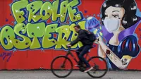 Pengendara sepeda melewati grafiti bertema virus corona COVID-19 yang bertuliskan ‘Happy Easter’ pada dinding di Hamm, Jerman, Senin (13/4/2020). Kasus COVID-19 tertinggi di dunia ditempati oleh Amerika Serikat, Spanyol, Italia, Prancis, Jerman, dan China. (AP Photo/Martin Meissner)
