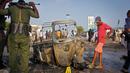Tentara dan seorang anak berdiri dekat puing-puing kendaraan di lokasi ledakan bom mobil dekat pos pemeriksaan parlemen dan Kementerian Dalam Negeri di Ibu Kota Somalia, Mogadishu, Minggu (25/3). Serangan menewaskan empat orang. (AP/Farah Abdi Warsameh)
