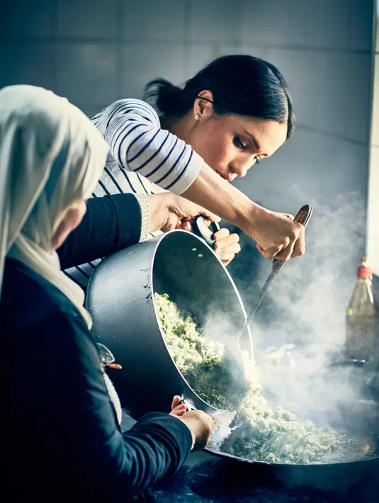Meghan Markle membantu memasak nasi bersama anggota Hubb Community Kitchen di London (19/7). Komunitas ini beranggotakan perempuan, yang merupakan korban kebakaran blok apartemen Menara Grenfell pada Juni 2017. (Jenny Zarins/Kensington Palace via AP)