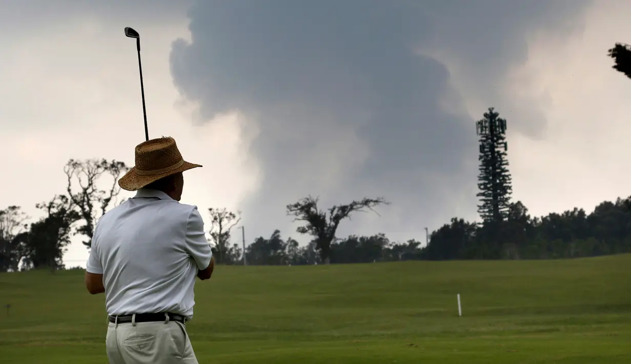 Ken McGilvray bermain golf saat kepulan asap abu vulkanik berembus dari puncak gunung Kiluaea di Volcano, Hawaii (16/5). Sekitar 2.000 orang telah dievakuasi dari rumah mereka termasuk 300 yang tinggal di tempat penampungan. (AP Photo/Jae C. Hong)