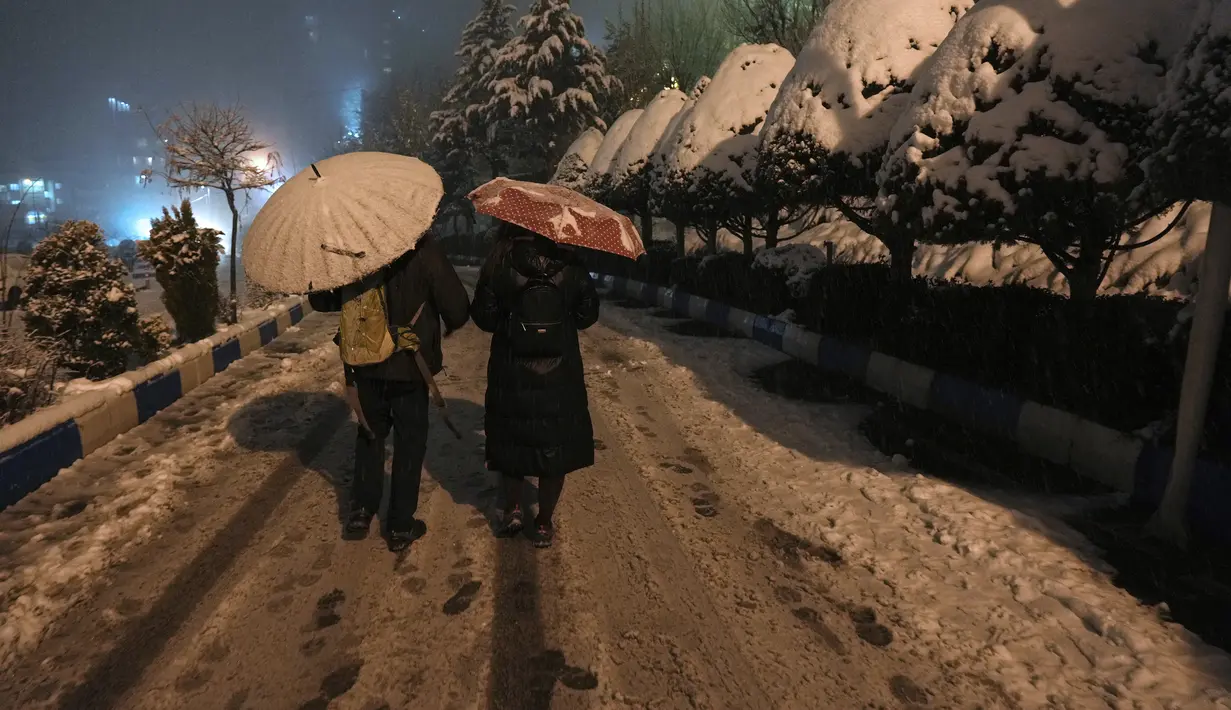 Orang-orang menggunakan payung saat salju turun di Kompleks Olahraga dan Rekreasi Tochal yang bergunung-gunung di Teheran utara, Iran (24/12/2022). Salju dan hujan membawa kebahagiaan bagi banyak orang yang khawatir kekurangan air di Iran, negara yang telah mengalami kekeringan selama beberapa dekade. (AP Photo/Vahid Salemi)