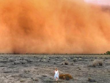 Foto  yang diambil 17 Januari 2020 dan diterima 20 Januari memperlihatkan seorang anak berlari menuju badai debu di Mullengudgery, New South Wales. Badai debu melanda banyak bagian barat New South Wales Australia ketika kekeringan berkepanjangan berlanjut. (Handout/Courtesy of Marcia Macmillan/AFP)