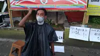 Ari Ahmad Riadi (25), salah seorang tukang cukur sekaligus seniman kota Garut, membuat pertunjukan dengan memotong rambutnya sendiri menggunakan sebuah mesin cukur, sebagai bentuk keprihatinan pemberlakuan PPKM Darurat saat ini. (Liputan6.com/Jayadi Supriadin)