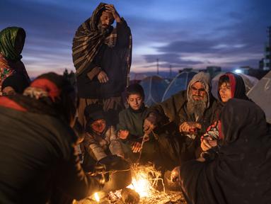 Sebuah keluarga menghangatkan diri di luar kantor Direktorat Bencana tempat mereka berkemah, di Herat, Afghanistan (29/11/2021). Sekitar 2000 pengungsi meninggalkan desa Allahyar di provinsi Ghor karena kekeringan dan mencari bantuan dari pemerintah daerah di Herat. (AP Photo/Petros Giannakouris)