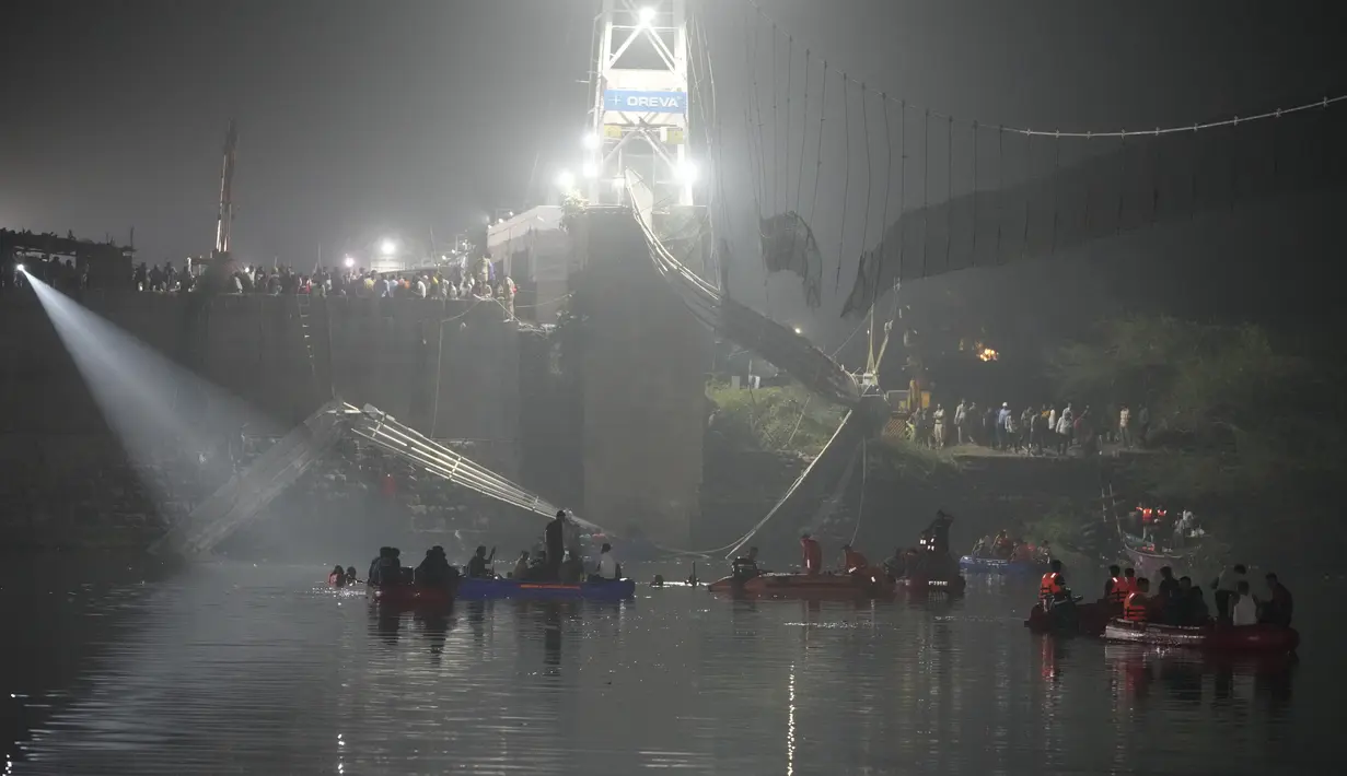 Tim penyelamat di kapal mencari di sungai Machchu di sebelah jembatan kabel yang runtuh di kota Morbi di negara bagian barat Gujarat, India, Senin, 31 Oktober 2022. Jembatan gantung kabel berusia seabad runtuh ke sungai Minggu malam, menyebabkan ratusan orang terjun. di dalam air, kata para pejabat. (AP/Ajit Solanki)