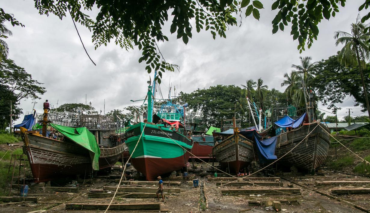 Para pekerja berjalan melewati kapal-kapal yang sedang diperbaiki di galangan kapal di tepi Sungai Yangon, yang terletak di pinggiran Yangon, Myanmar (30/7/2019). (AFP Phot/Sai Aung Main)