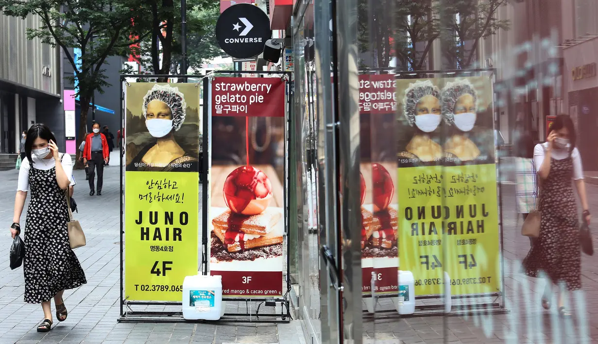 Seorang wanita yang mengenakan masker untuk membantu melindungi dari penyebaran virus corona COVID-19 berjalan melewati iklan toko rambut di sebuah distrik perbelanjaan di Seoul, Korea Selatan, Kamis (2/7/2020). (AP Photo/Ahn Young-joon)