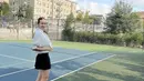 Gaya sporty Enzy Storia di lapangan tenis. Ia mengenakan cropped jacket tenis berwarna putih, dipadu rok hitam, dan sneakers putih. [Foto: Instagram/enzystoria]