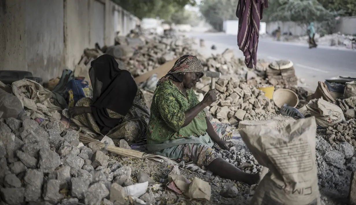 Idjele (kanan), 38, dan bibinya yang sudah tua duduk di antara batu untuk dihancurkan dekat Cite International des Affaires, N'Djamena, Chad, 12 April 2021. Dalam debu dan panas, wanita Chad menghancurkan kerikil untuk memenuhi kebutuhan. (MARCO LONGARI/AFP)