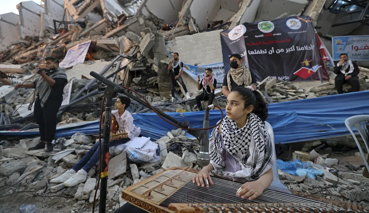 Seorang gadis Palestina memainkan alat musik saat tampil di puing-puing Menara Hanadi di Kota Gaza (2/6/2021). Acara diselenggarakan oleh Komite Pemuda dan Kebudayaan Palestina lebih dari seminggu setelah gencatan senjata mengakhiri 11 hari permusuhan antara Israel dan Hamas. (AFP Photo/Mohammed Abe