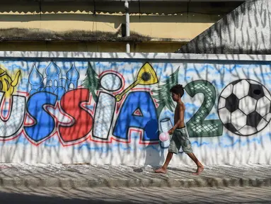 Seorang anak laki-laki melewati mural Piala Dunia 2018 di dinding jalanan Camboata, Rio de Janeiro, Brasil, Kamis (31/6). (Fabio TEIXEIRA/AFP)