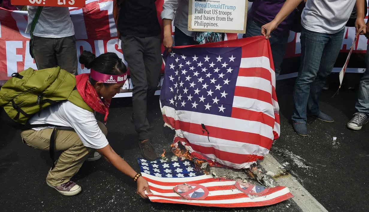 Aktivis membakar bendera AS dengan wajah Presiden terpilih Donald Trump di depan kedutaan AS, Manila, Filipina (20/1). Pengunjuk rasa menuding Presiden terpilih AS itu memiliki sifat seksisme, rasisme dan xenophobia. (AFP Photo/Ted Aljibe)