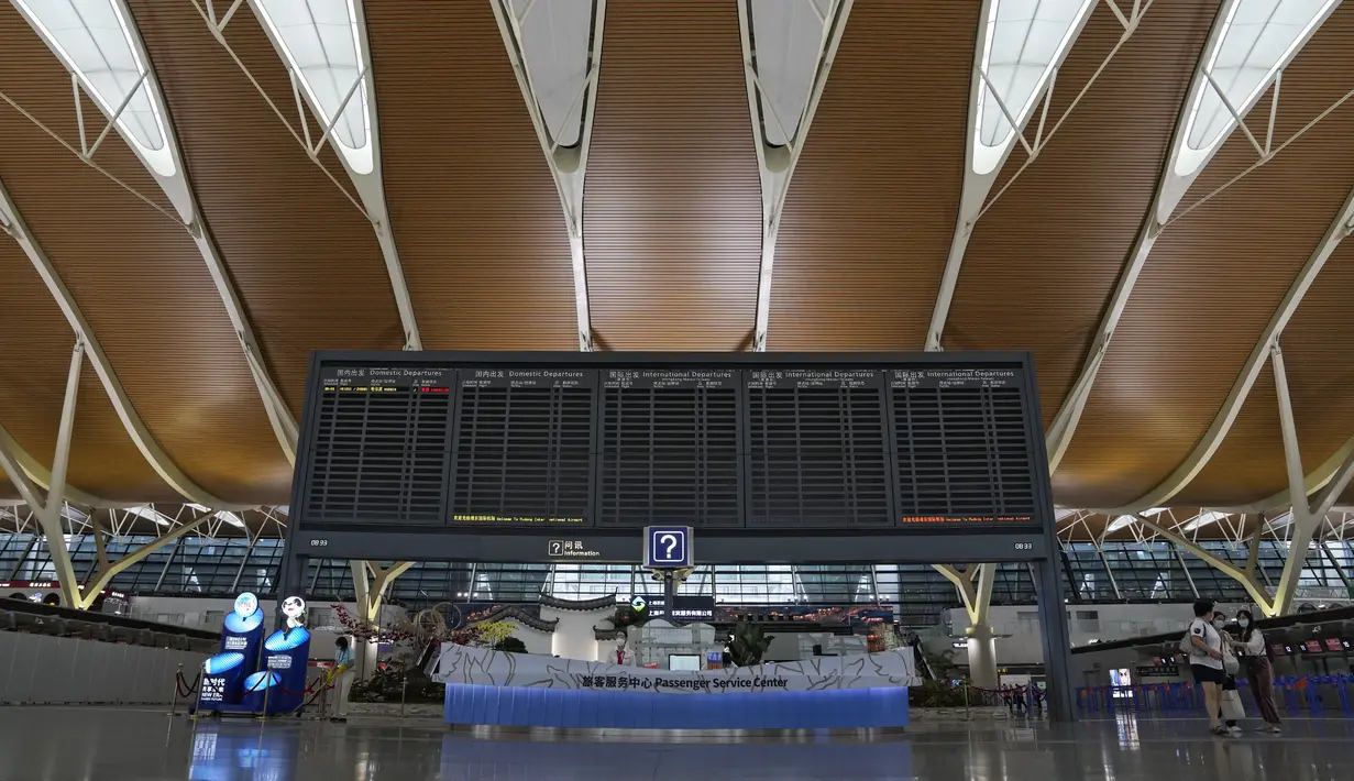 Penumpang berdiri di dekat papan informasi penerbangan domestik dan internasional di Bandara Internasional Pudong, Shanghai, Minggu (25/7/2021). China telah menutup jalur kereta api dan pelabuhan, serta membatalkan jadwal penerbangan sebelum topan In-Fa diperkirakan mendarat. (AP Photo/Andy Wong)