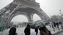 Pejalan kaki berjalan di dekat Menara Eiffel saat turun salju di Paris, Prancis, (6/2). Badan cuaca nasional Prancis Meteo France mengatakan sekitar setengah negara di eropa siaga atas bahaya tingkat salju dan es yang berbahaya. (AP Photo / Francois Mori)