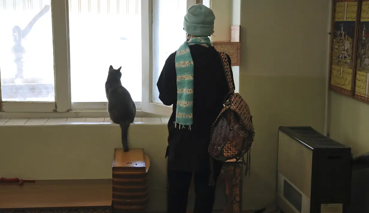 Pengunjung berdiri di samping seekor kucing yang memandang ke luar jendela, di Museum Kucing Persia di Teheran, Iran, pada 5 Desember 2021. Didirikan di sebuah rumah tua pada tahun 2020, Museum Kucing Persia ini berawal dari kafe serba guna dan pameran kucing. (AP Photo/Vahid Salemi)