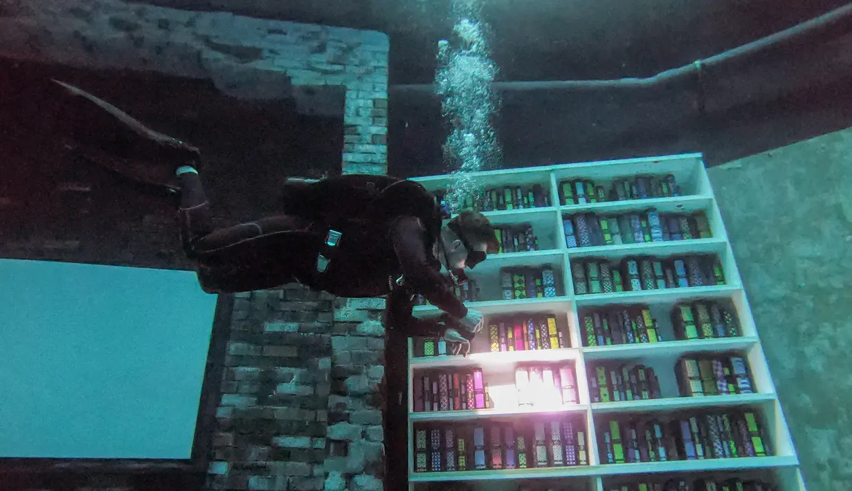 Seorang penyelam melihat-lihat buku tiruan saat menyelam di Deep Dive Dubai, Dubai, Uni Emirat Arab, 10 Juli 2021. Deep Dive Dubai adalah kolam renang terdalam di dunia. (GIUSEPPE CACACE/AFP)