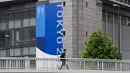 Seseorang dengan masker berjalan di jembatan penyeberangan saat spanduk Tokyo 2020 terlihat di sisi gedung di Tokyo, Rabu (23/6/2021). Olimpiade Tokyo dimulai pada 23 Juli dan penyelenggara mengizinkan penonton lokal menghadiri venue pertandingan dengan kapasitas 50 persen. (AP Photo/Kiichiro Sato)