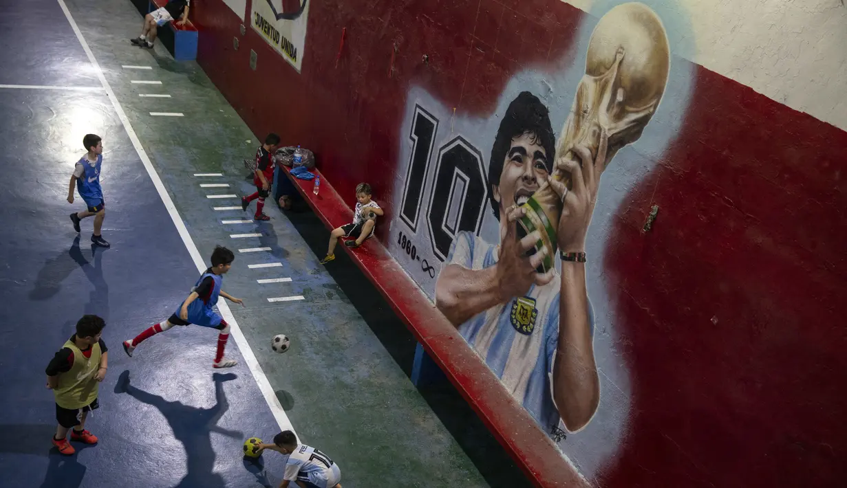 Anak-anak bermain sepak bola di dekat mural yang menampilkan mendiang legenda sepak bola dunia, Diego Maradona di klub "Juventud Unida" di Buenos Aires, Argentina, Rabu (24/11/2021). Peringatan pertama kematian Maradona digelar pada 25 November 2021. (AP Photo/Rodrigo Abd)