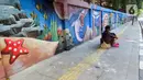 Warga duduk di trotoar dekat mural bertema biota laut yang menghiasi dinding di kawasan Cideng, Jakarta, Rabu (29/11/2023). Mural dibuat guna memperindah sekaligus penataan kawasan Kelurahan Cideng, Jakarta Pusat. (Liputan6.com/Herman Zakharia)