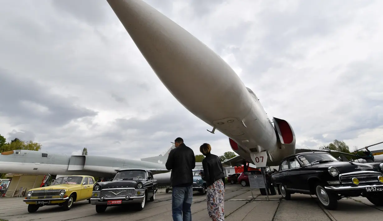 Pengunjung melihat mobil dan pesawat terbang selama hari pembukaan festival mobil retro OldCarLand di Kiev (27/4). Pameran kendaraan jadul ini digelar dari 27 April hingga Mei, 1, 2018. (AFP Photo/Sergei Supinsky)