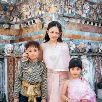 Dalam foto yang diabadikan di salah satu kuil paling ikonik di Bangkok tersebut, Rachel tampil serasi bersama kedua buah hatinya, Xabiru dan Chava, mengenakan chut thai, busana tradisional Thailand, dengan sentuhan warna lembut yang memancarkan kesan anggun sekaligus hangat sebagai keluarga. [@rachelvennya].